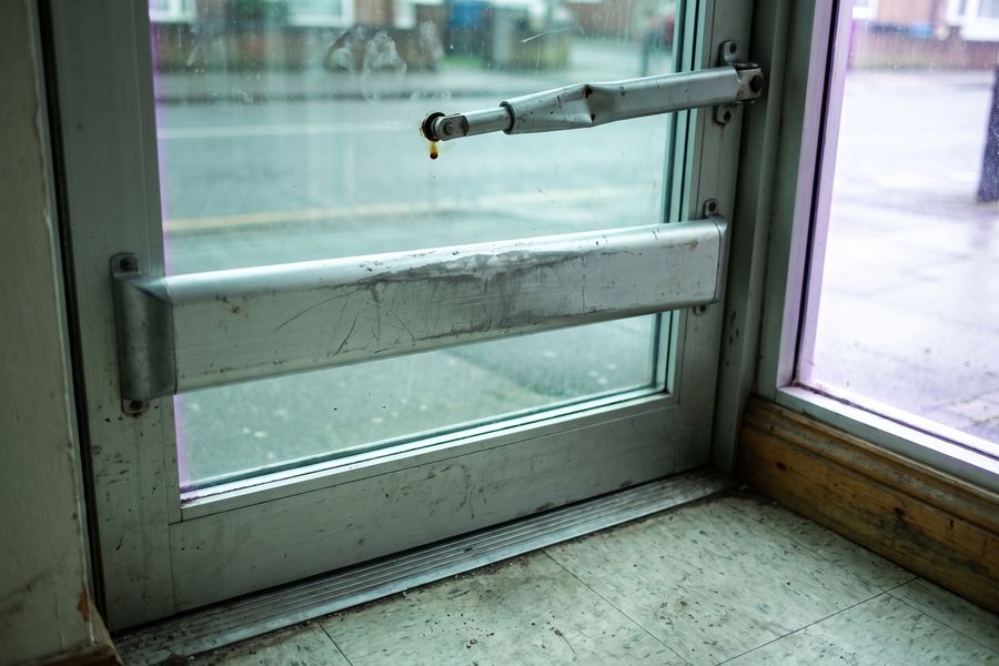The interior push bar of a commercial aluminium and glass storefront door with an overhead closer